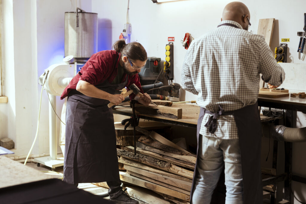 Manufacturer carving wood using chisel and hammer, wearing safety glasses